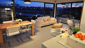 Een moderne woonkamer met een groot raam, een eethoek met een houten tafel, en een keuken met een spoelbak en aanrecht.