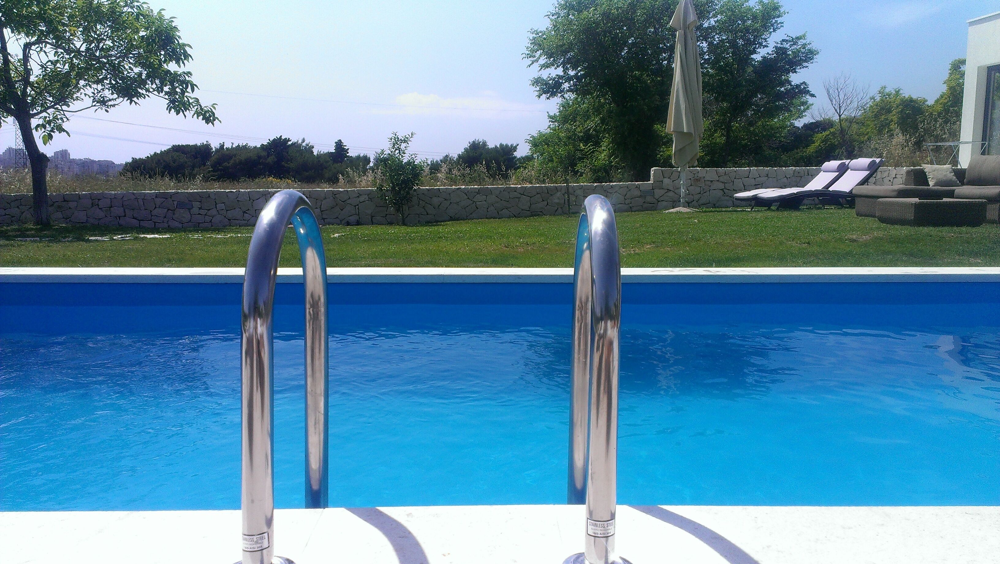 Una piscina con escalera metálica y un muro de piedra al fondo.