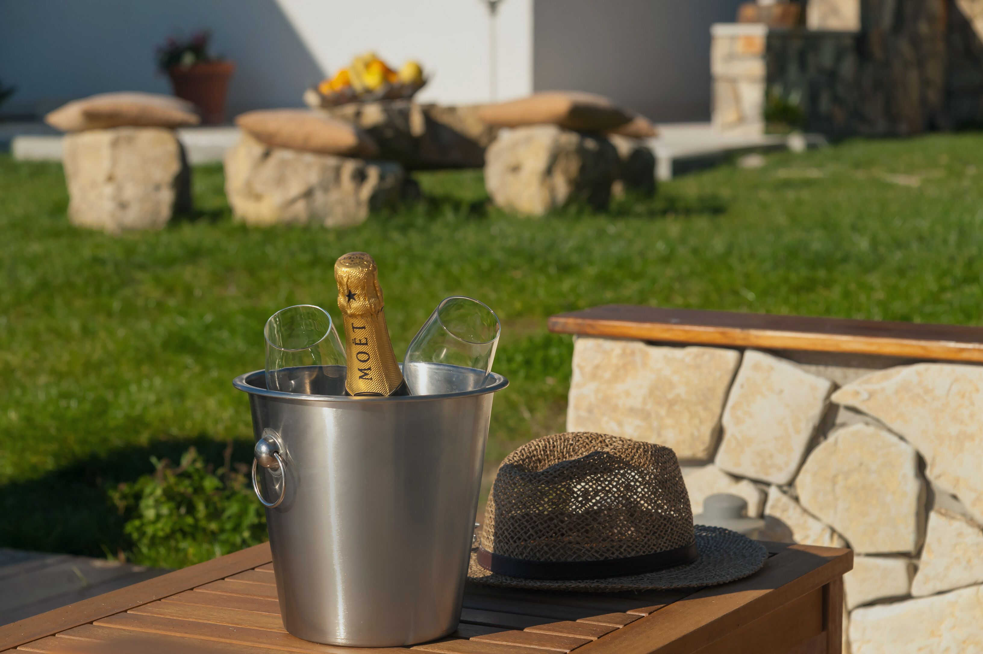 A metal bucket with a bottle and glasses on a wooden table outdoors.