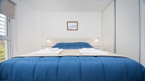 A neatly made bed with a blue comforter and white linens, a framed picture on the wall, and bedside lamps. - Rent Venezuela CA5 (Córdoba)