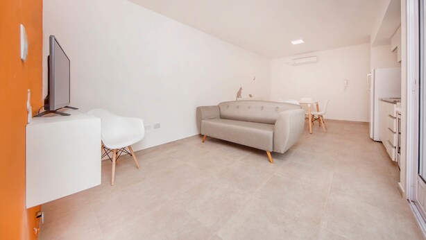 A modern, well-lit living area with a sofa, a small table, and a TV on a white cabinet. - Rent Venezuela CA5 (Córdoba)