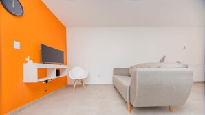 A modern living room with a grey sofa, a white chair, and a flat-screen TV mounted on an orange wall. - Rent Venezuela CA5 (Córdoba)