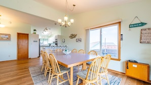 A spacious dining area with a wooden table and chairs, a chandelier, and a view of the beach through a large window. - Duck R Way - Poteskeet, Ocean View, 260 Yds to Beach, Pool, Hot Tub, Walk to Downtown Duck (Duck)