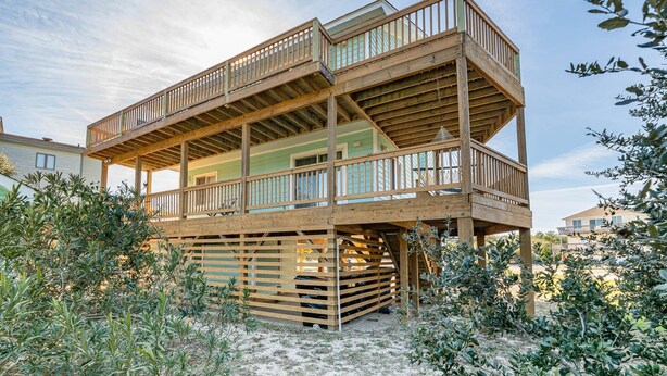 A multi-level wooden deck structure with railings, elevated above ground, surrounded by vegetation. - Duck R Way - Poteskeet, Ocean View, 260 Yds to Beach, Pool, Hot Tub, Walk to Downtown Duck (Duck)