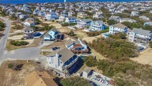 An aerial view of a coastal residential area with houses, a swimming pool, and a lighthouse in the background. - Duck R Way - Poteskeet, Ocean View, 260 Yds to Beach, Pool, Hot Tub, Walk to Downtown Duck (Duck)