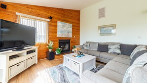 A living room with a TV, sofa, fireplace, and wooden walls. - Duck R Way - Poteskeet, Ocean View, 260 Yds to Beach, Pool, Hot Tub, Walk to Downtown Duck (Duck)