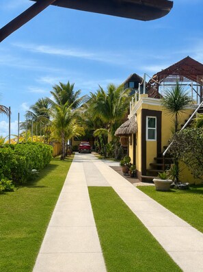 A pathway leading to a building with a thatched roof, surrounded by palm trees and a red car parked in front.