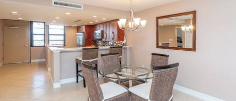 A dining area with wicker chairs, a glass table, and a kitchen in the background.