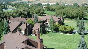 A residential area with multiple houses, a golf course, and a hilly landscape in the background.