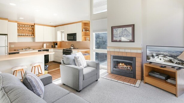 A modern kitchen with white cabinets, a dining area with a bar, a fireplace, and a television.