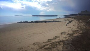 A beach with a sandy shore, a rocky outcrop, and a building on the right. - Across from Mayo beach walk to downtown! (Wellfleet)