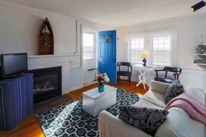 A living room with a fireplace, a blue door, a television, and a coffee table with a vase.