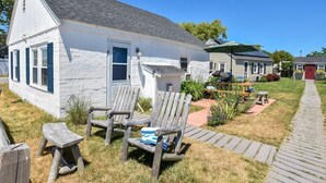 A white building with a sloped roof and a small porch area with wooden chairs and a table. - Across from Mayo beach walk to downtown! (Wellfleet)