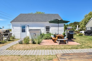 A single-story house with a front door, a small porch, and a patio area with a table and chairs.