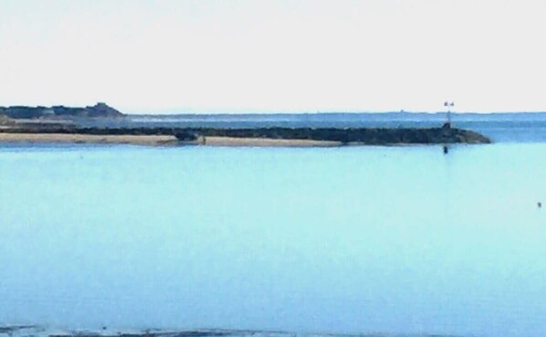 A coastal scene with a lighthouse on a small island, calm water, and a distant shoreline.