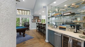 Een moderne keuken met een bar met glazen vitrine, houten vloeren en een pooltafel in de aangrenzende ruimte.