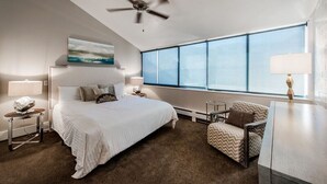 Ein modernes Hotelzimmer mit einem großen Bett, einem Deckenventilator, einem Fenster mit Blick, einem Sessel und einem Schreibtisch.