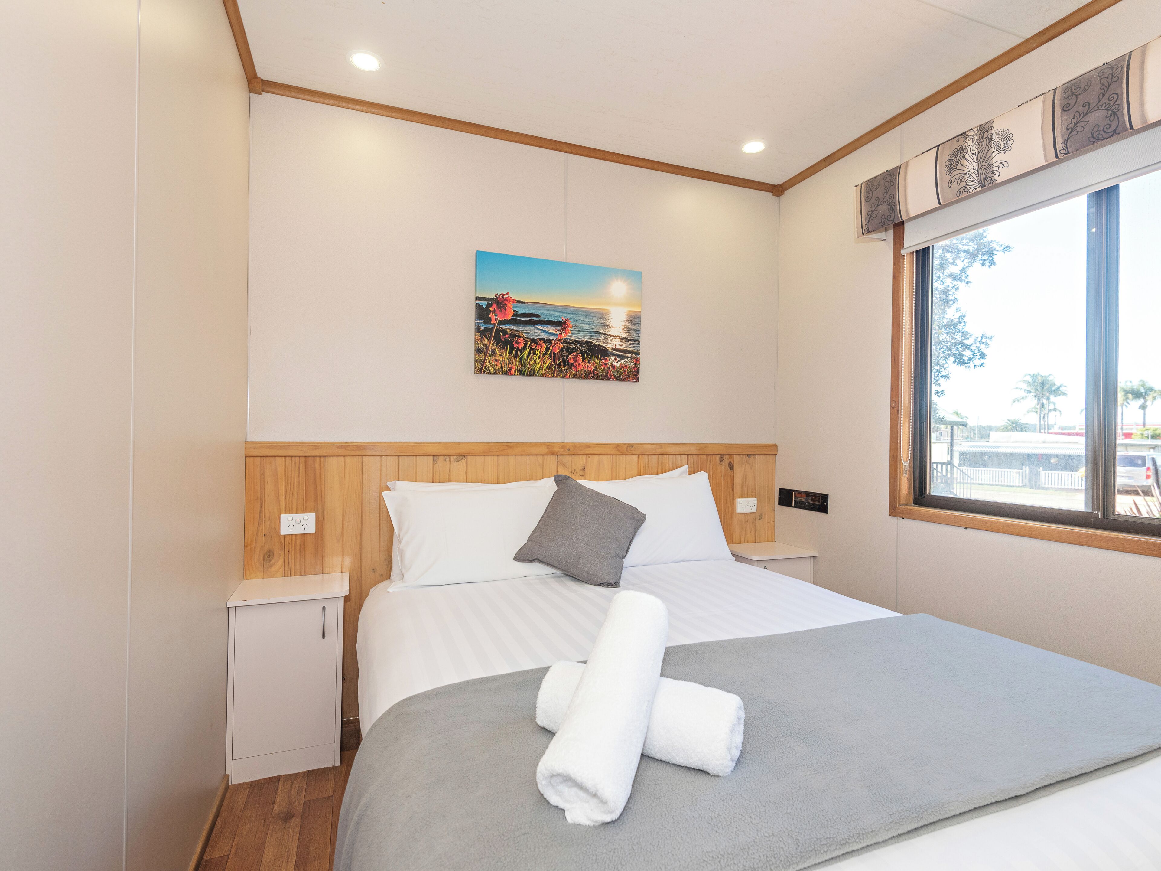 A hotel room with a bed, a nightstand, a painting, and a window.