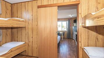 A room with wooden walls, bunk beds, a kitchenette, and a window with curtains.