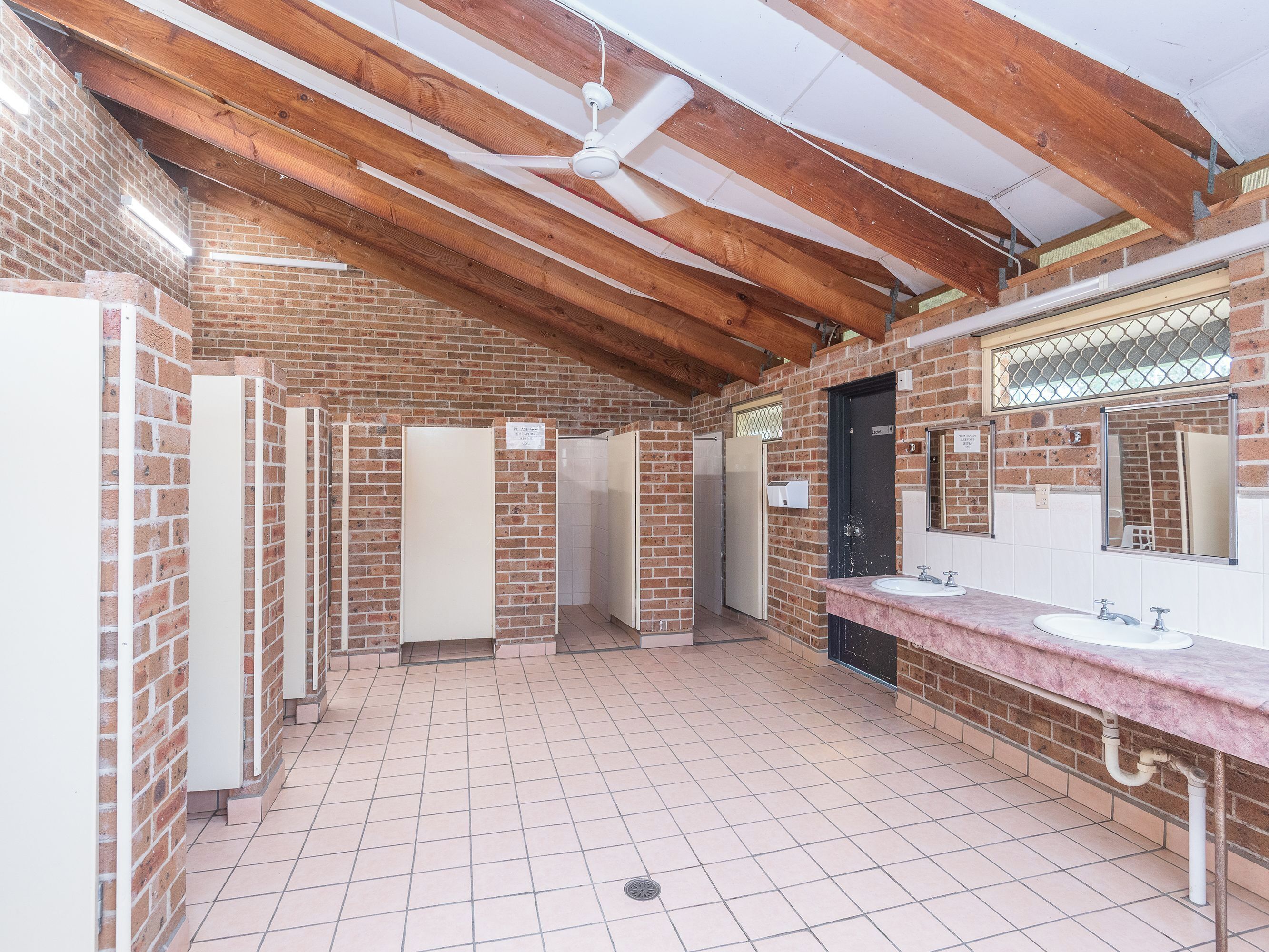 Een openbaar toilet met bakstenen muren, houten balken en betegelde vloeren.