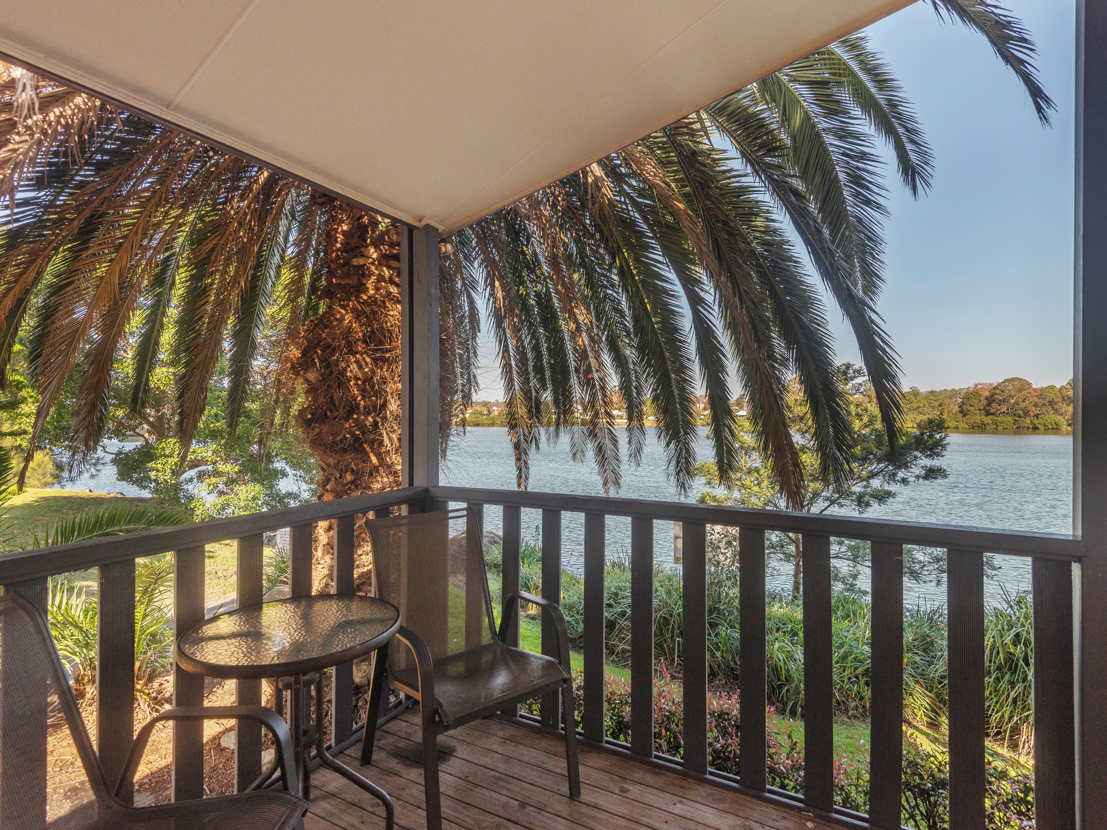 A covered outdoor area with a table and chairs, overlooking a body of water and palm trees.