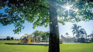 Een park met een speeltuin, een grote boom en een heldere lucht.