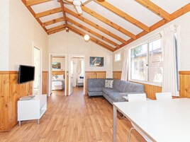Una habitación amplia con vigas de madera, televisión de pantalla plana, sofá, mesa de comedor y ventana con cortinas.