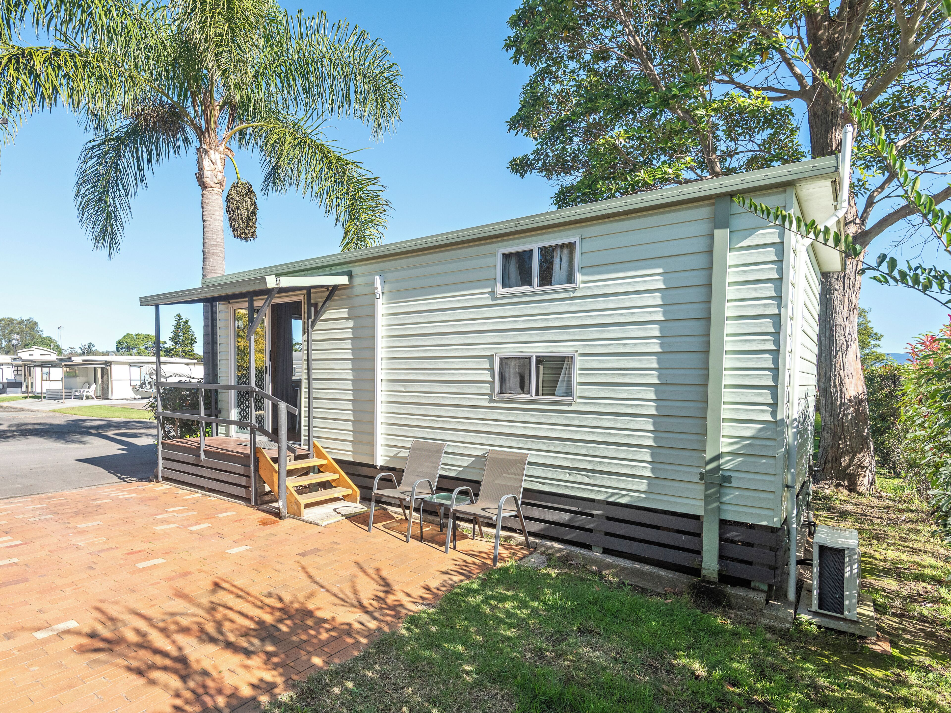 A mobile home with a porch, outdoor seating, and a tree in the background.