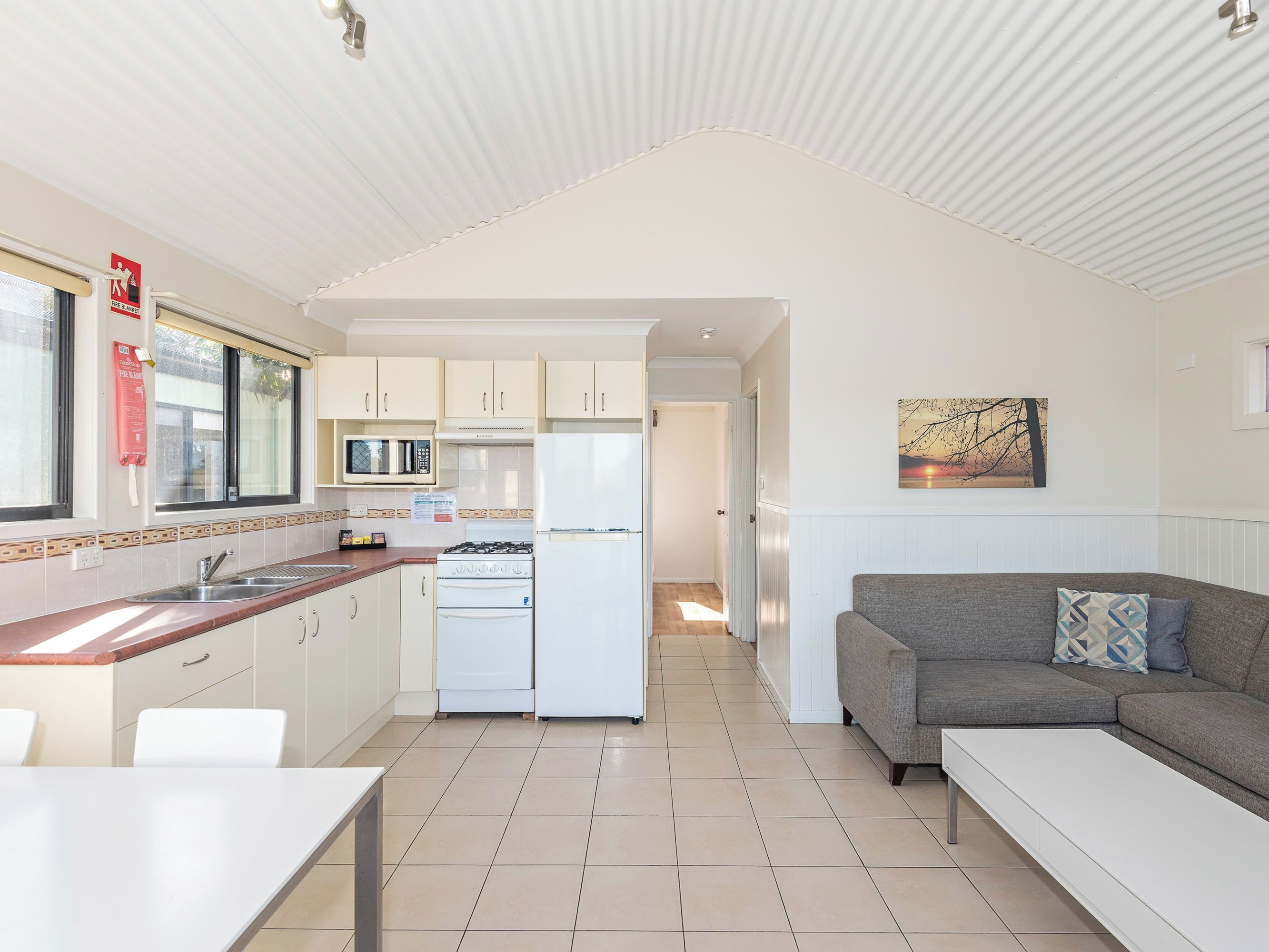 Cocina compacta con microondas, estufa y lavaplatos. En la zona de estar contigua, hay una mesa de comedor y un sofá.