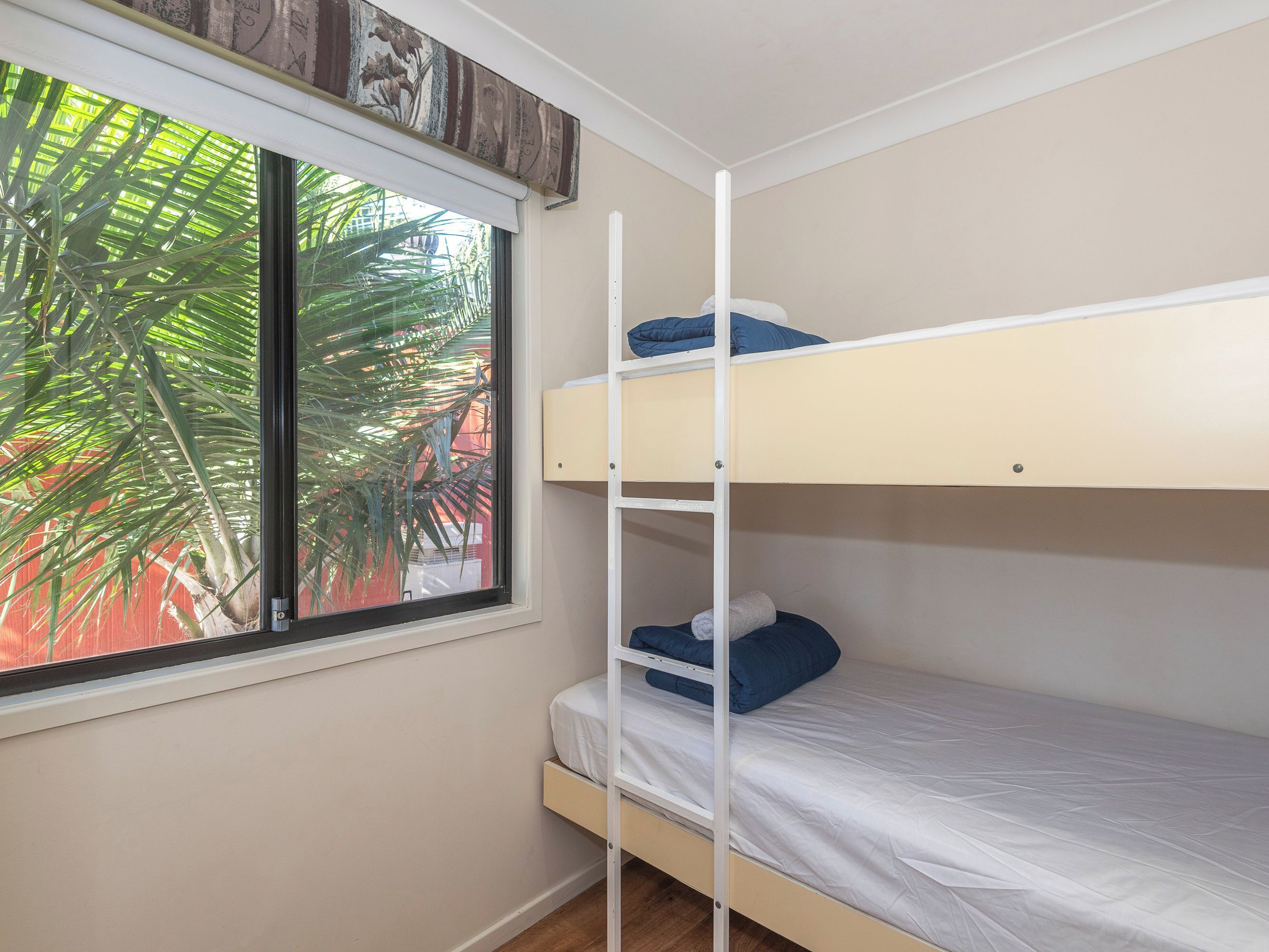 Een stapelbed met een raam, een houten plank en een plant erbuiten.