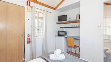 Un dormitorio con cama, escritorio con ordenador, silla y ventana.