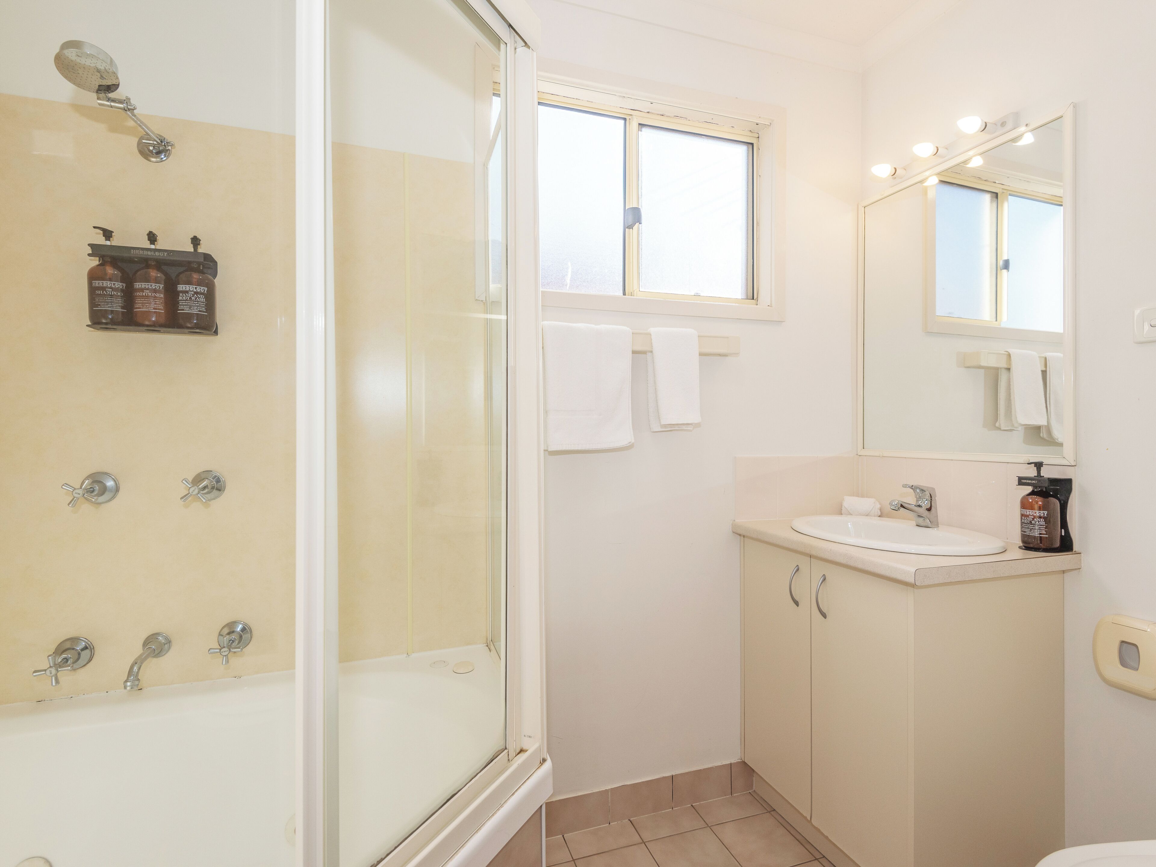 Une salle de bain avec une douche à parois de verre, un lavabo avec un miroir et une fenêtre située au-dessus du miroir.