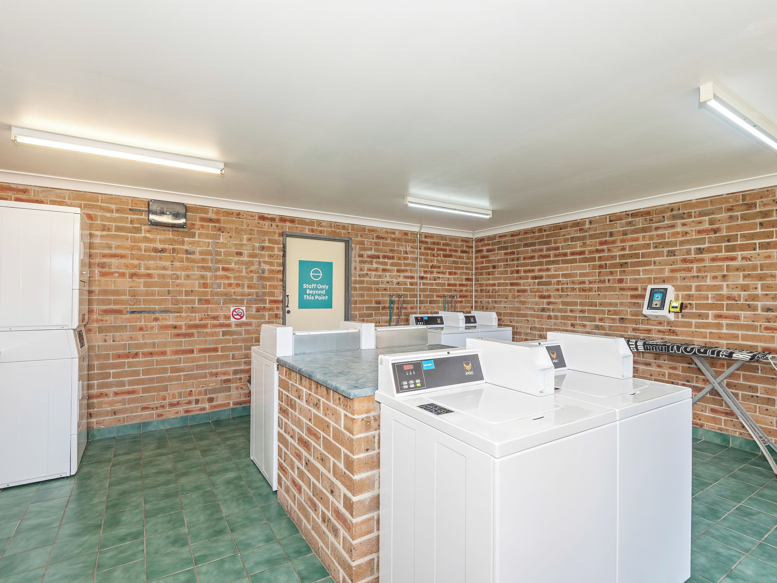Un cuarto de lavandería con varias lavadoras, un letrero que dice 'Solo personal' y un cartel de 'No fumar' en la pared.