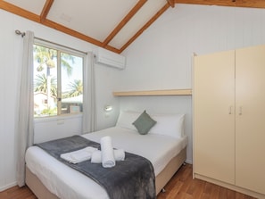 A bedroom with a bed, a wardrobe, a window with curtains, and an air conditioning unit. - Moruya Holiday Park (Moruya)