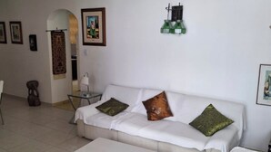 Een woonkamer met een witte bank, twee groene en één bruin kussen, een witte salontafel en een bijzettafeltje.