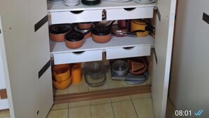 Een keukenkast met planken vol servies, pannen en keukengerei.