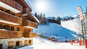 A wooden chalet with balconies, a ski slope in the background, and a ski lift.