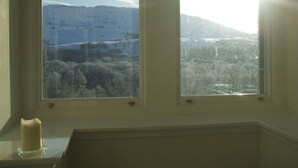 Ein Zimmer mit Fensterblick auf eine verschneite Landschaft, Bäume und ferne Berge.