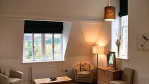 Ein gemütliches Zimmer mit einer Couch, einem Holztisch, einer Lampe und einem Schminktisch.
