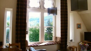 Ein Zimmer mit großem Fenster, Heizkörper, Fernseher und kleinem Tisch.