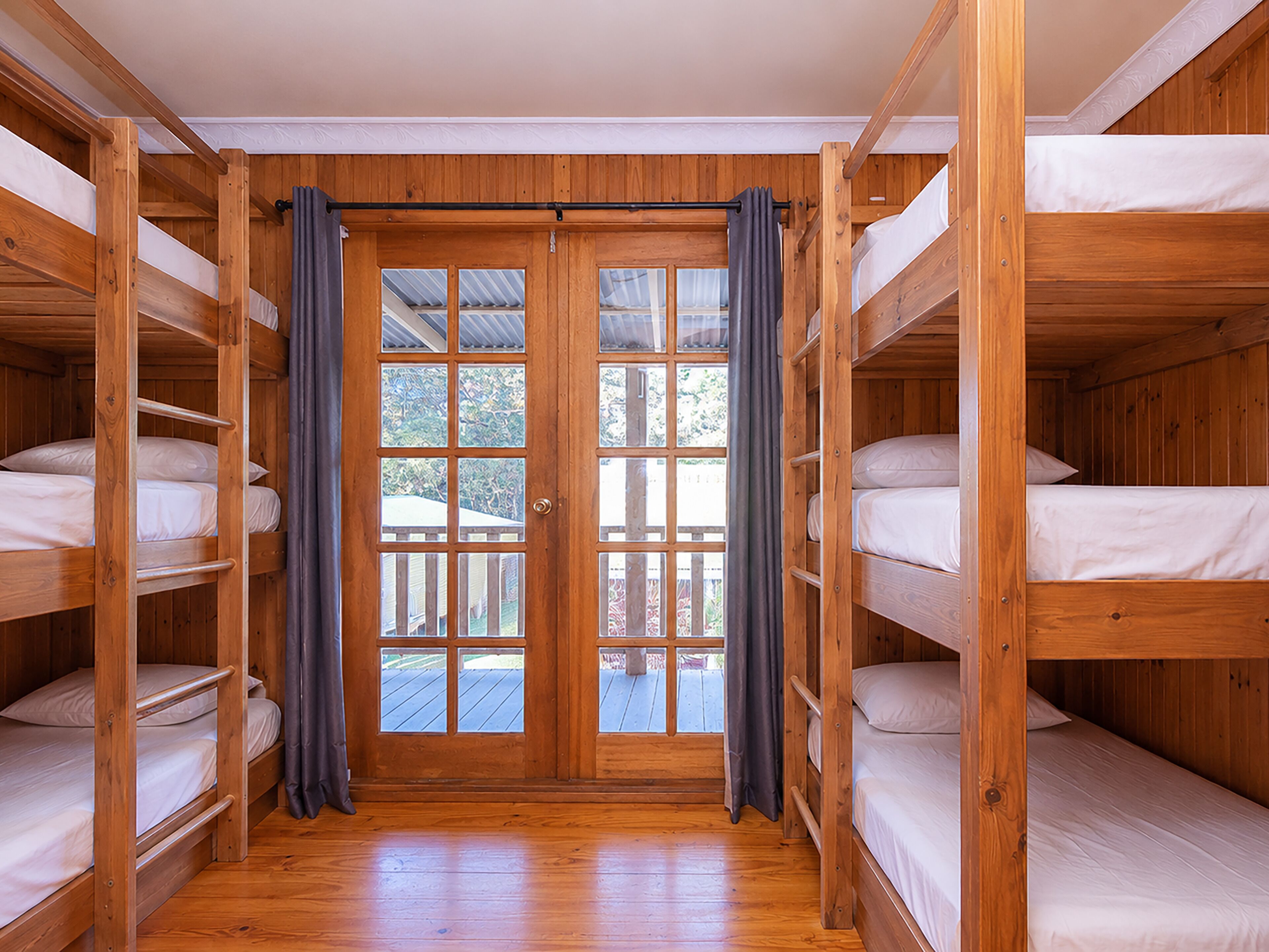 Une cabane en bois avec des lits superposés, une porte en bois avec des panneaux de verre, et une vue à travers la porte.