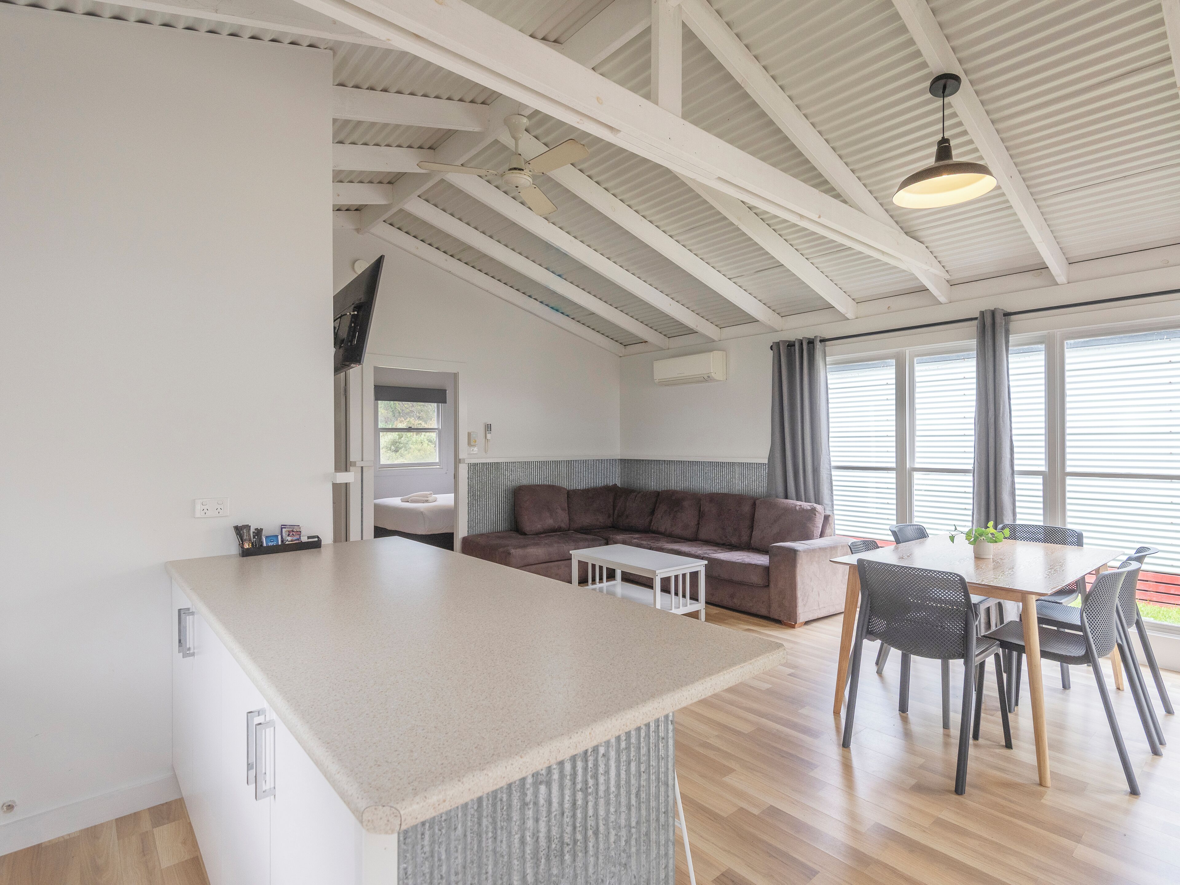 Una cocina moderna con una isla central, una zona de comedor con mesa y sillas, un sofá y un amplio ventanal con cortinas.