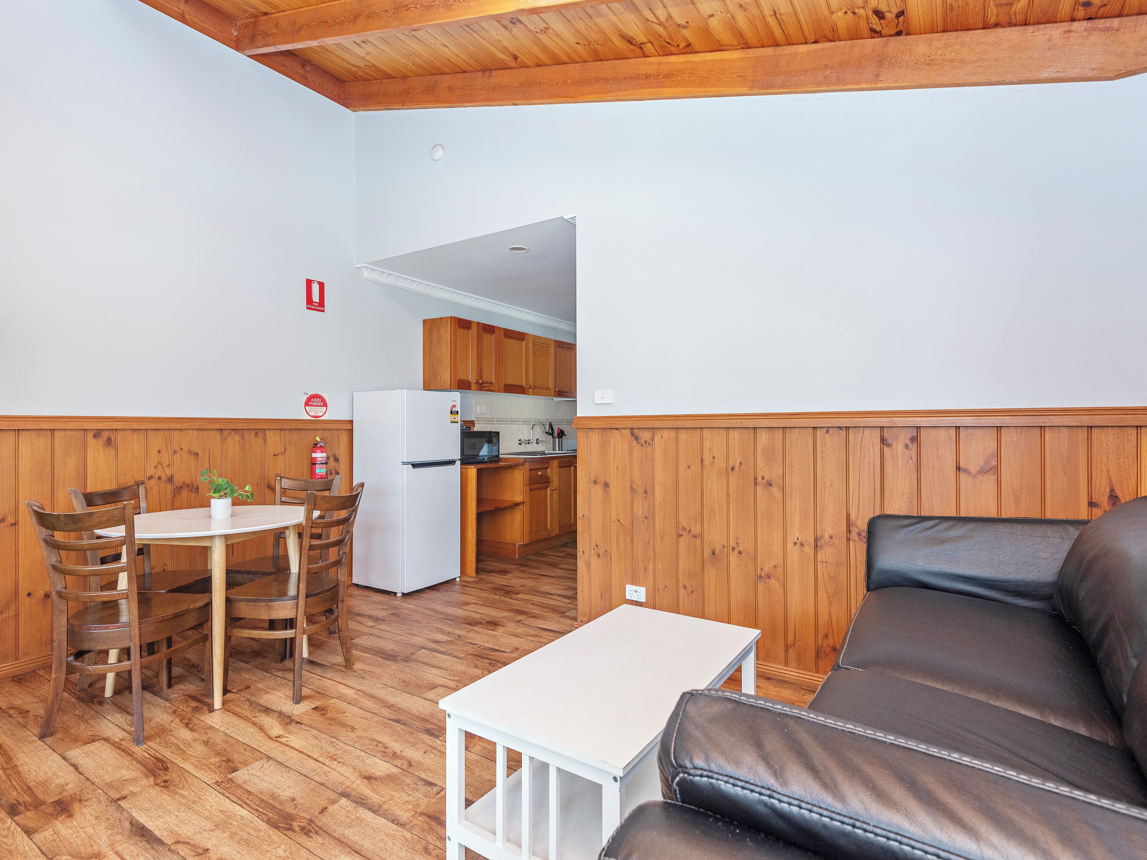 Una habitación con techo de madera, una mesa de comedor con sillas, un sofá y una kitchenette.