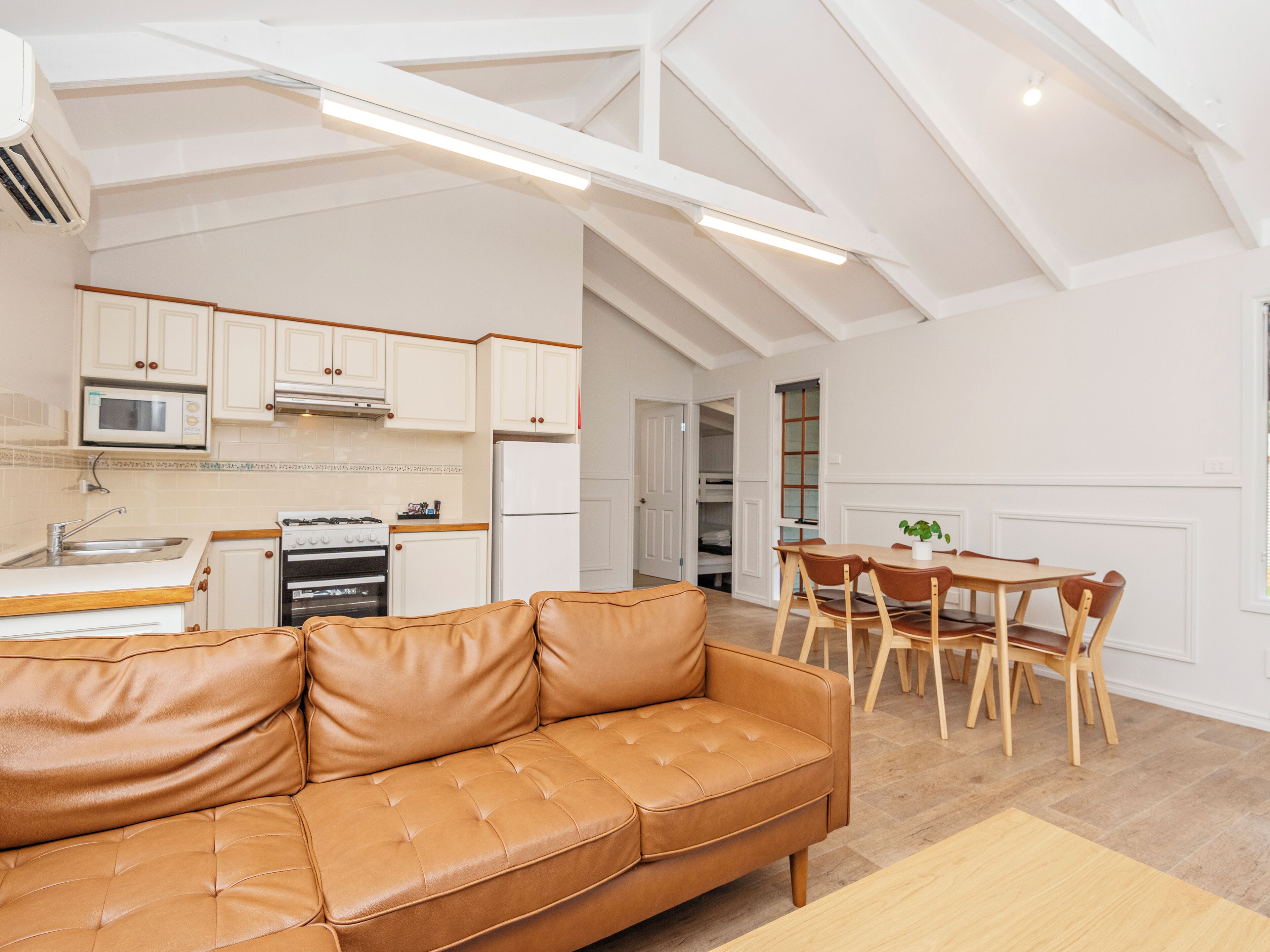 A modern kitchen with white cabinets, a dining area with wooden chairs, and a leather sofa.