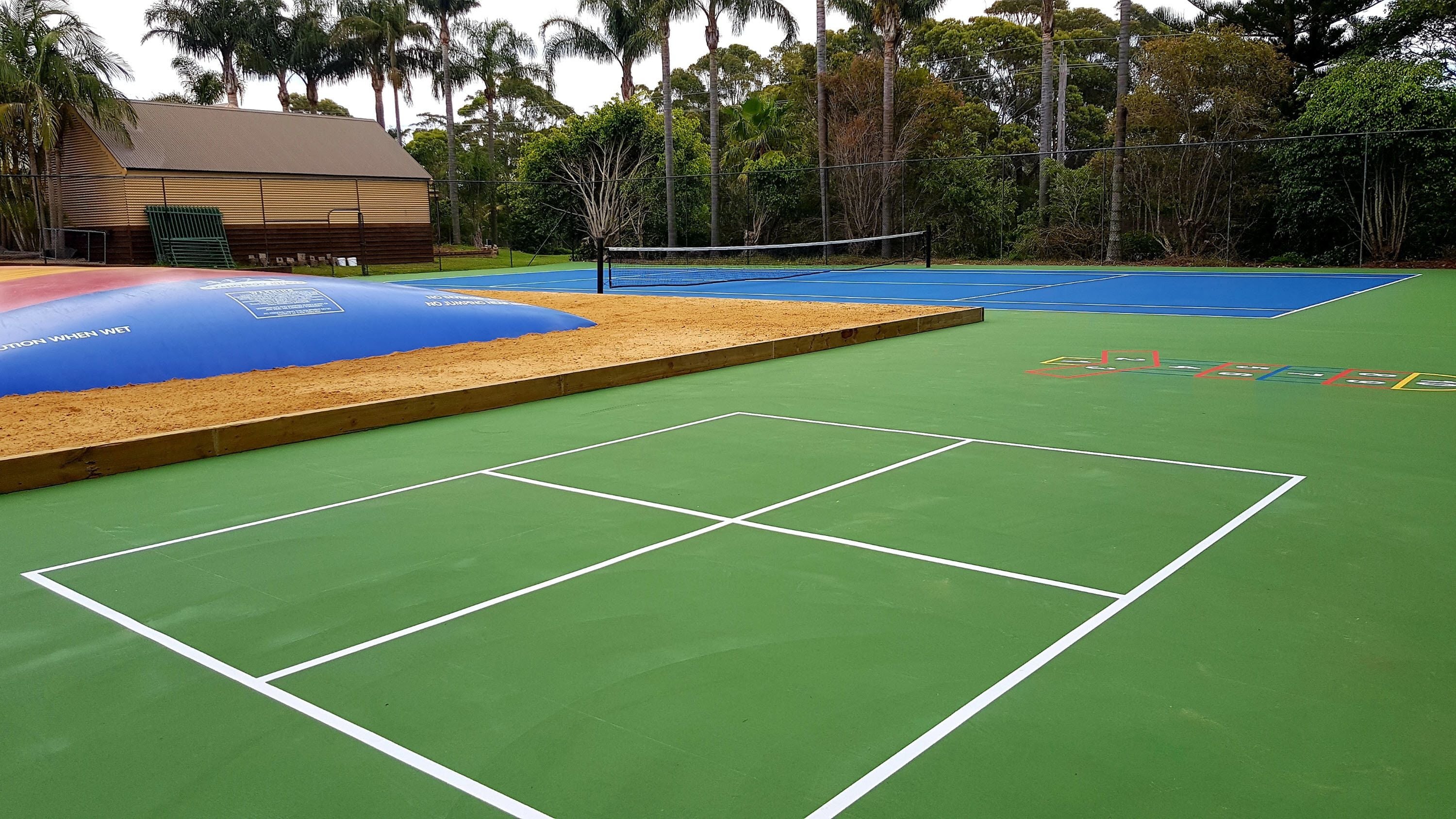 Ein Tennisplatz im Freien mit Netz, umgeben von Bäumen und einem Gebäude.