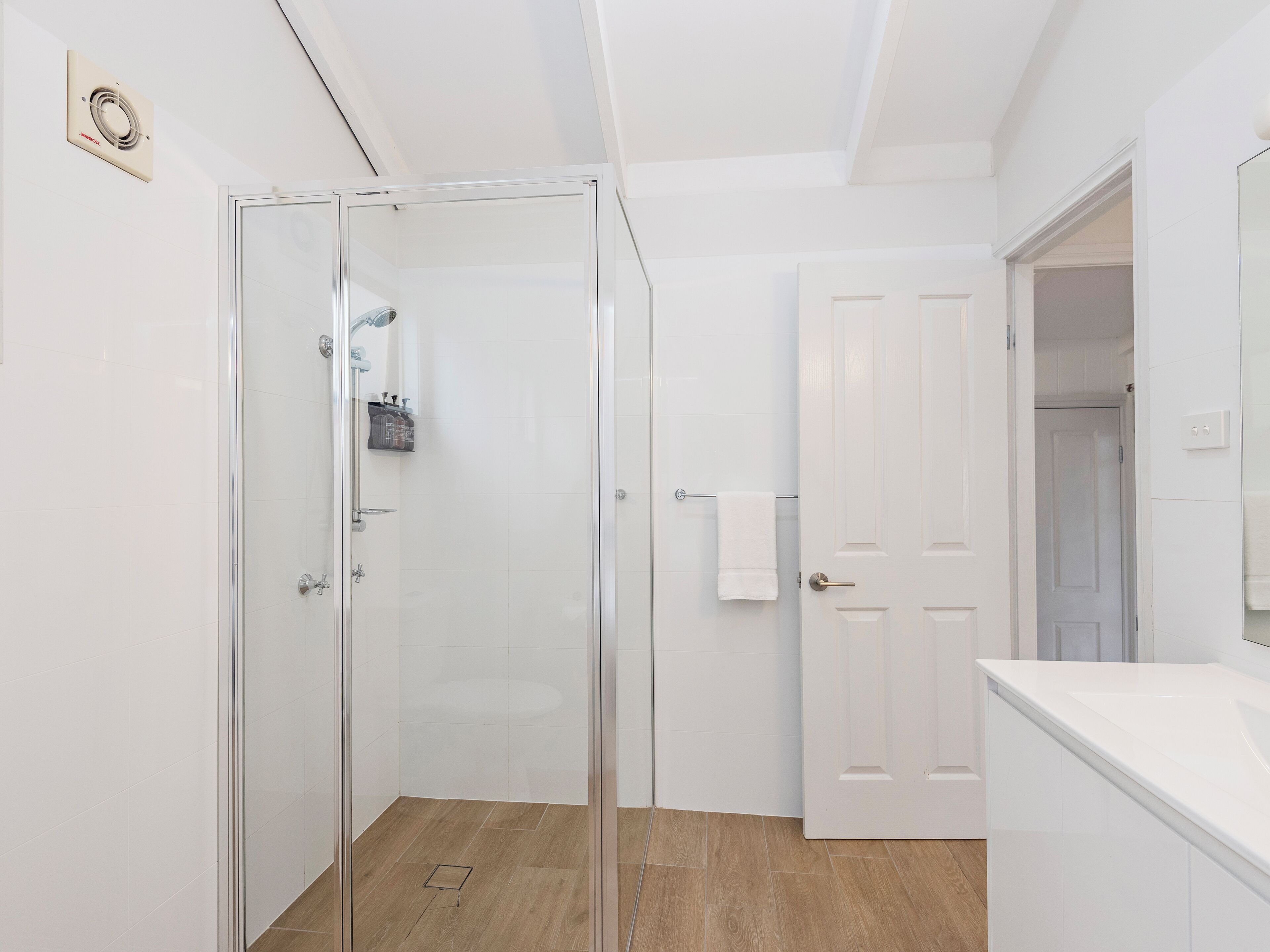A modern bathroom with a glass shower enclosure, a white door, and a wooden floor.