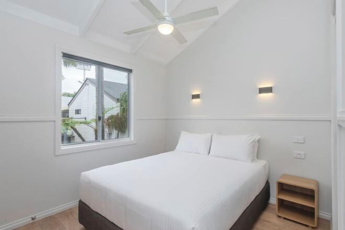 Ein Schlafzimmer mit Bett, Deckenventilator, Fenster und Nachttisch.