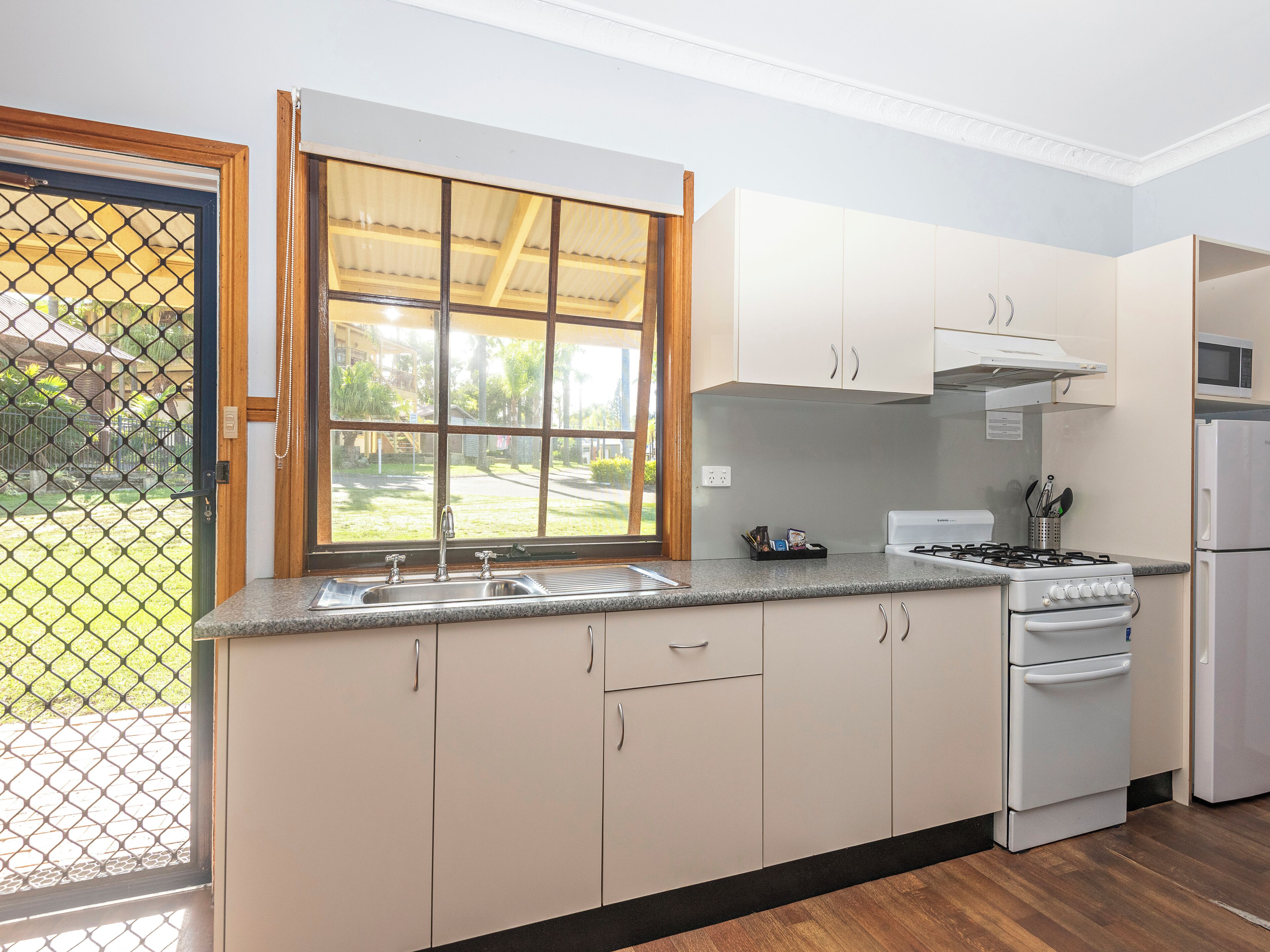 A kitchen with a window, a sink, cabinets, a stove, and a refrigerator.