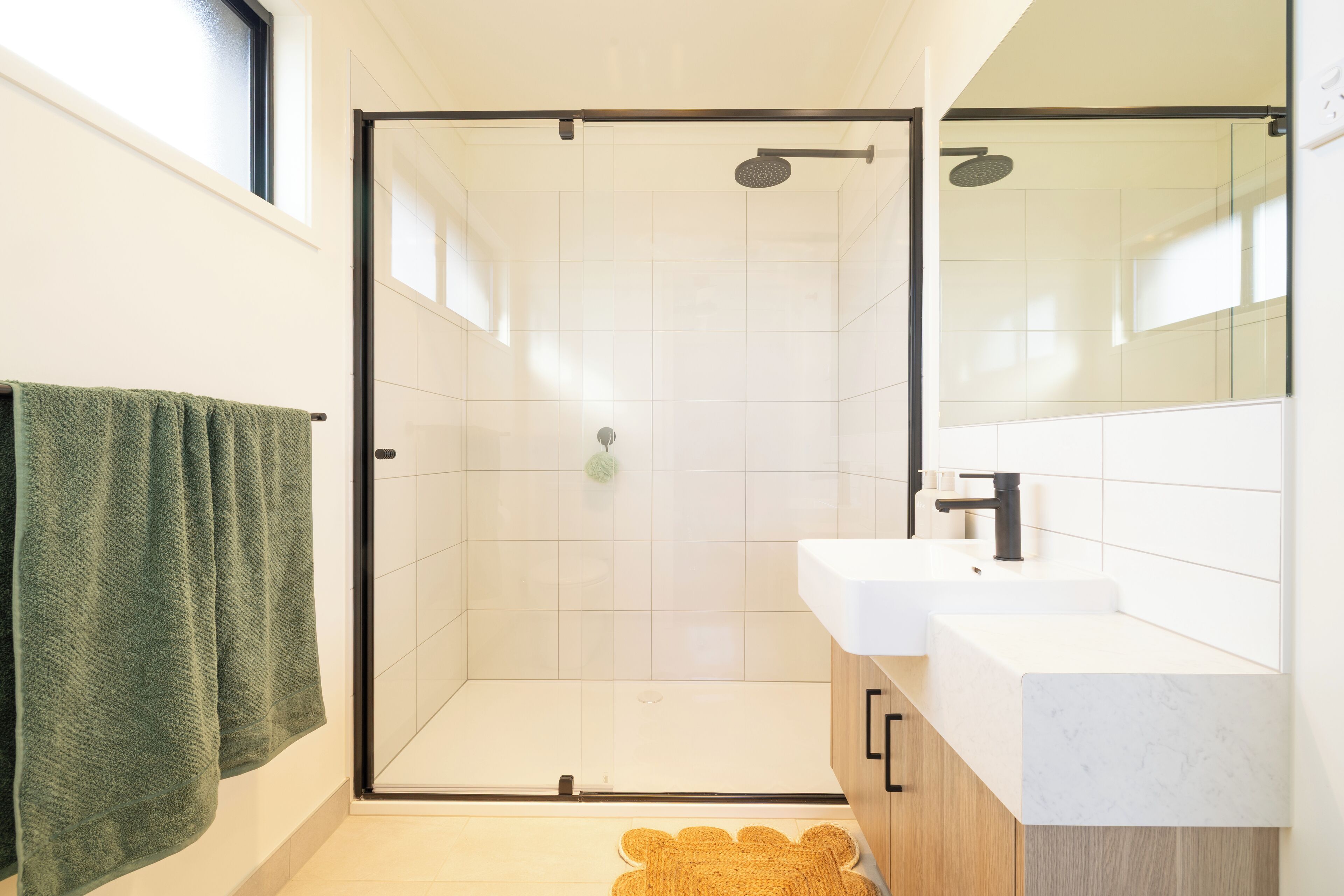 Un bany modern amb dutxa trencada per vidre, un lavabo blanc i una tovallola verda.