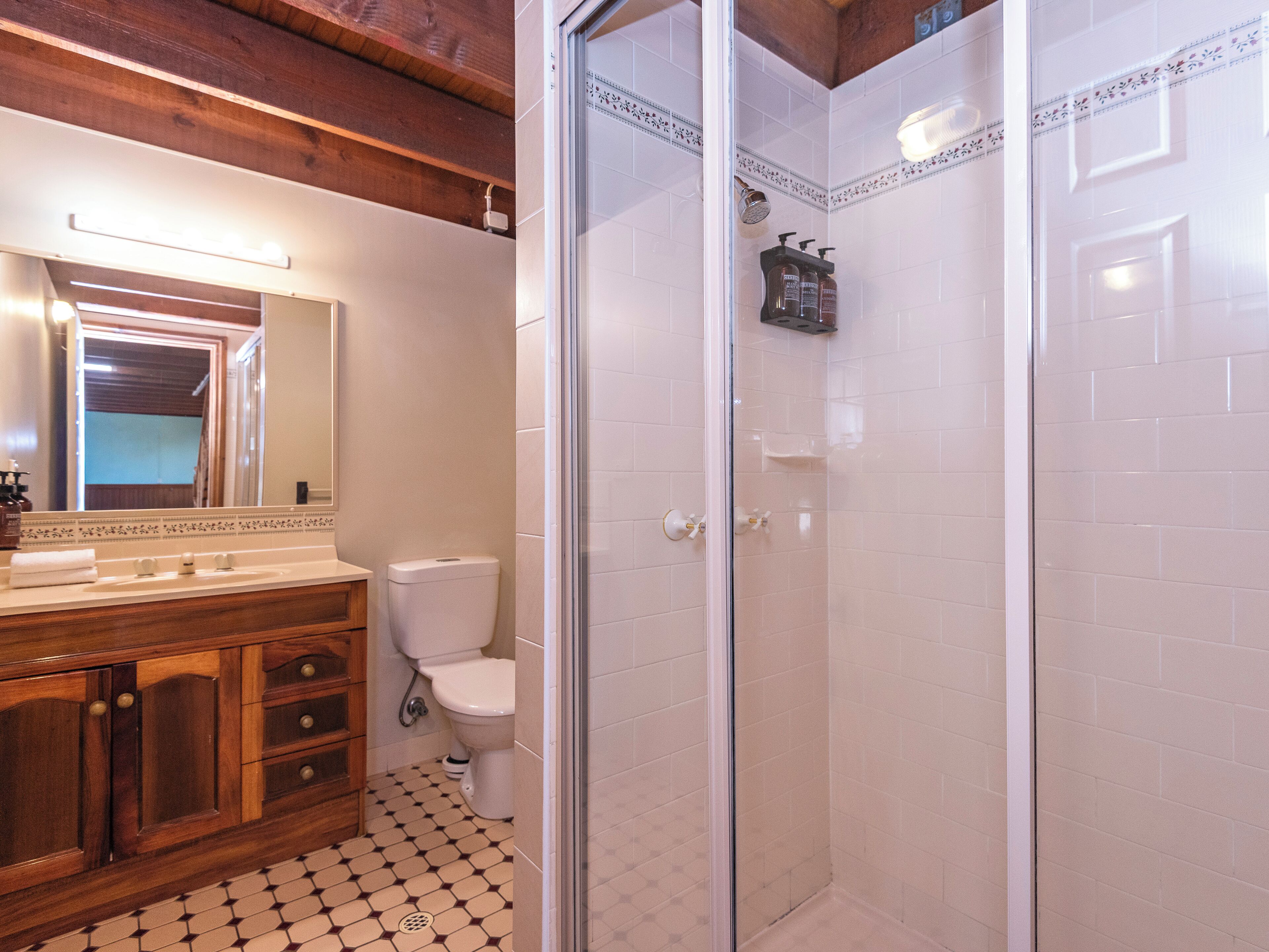 A bathroom with a wooden vanity, a toilet, a shower with glass doors, and a tiled floor.